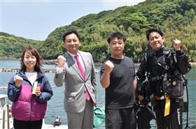 串浦港にて、海を背に集合写真を撮っている様子。山口知事が袈裟丸さんご夫妻、協力いただいたダイバーさんと並んで立っている。